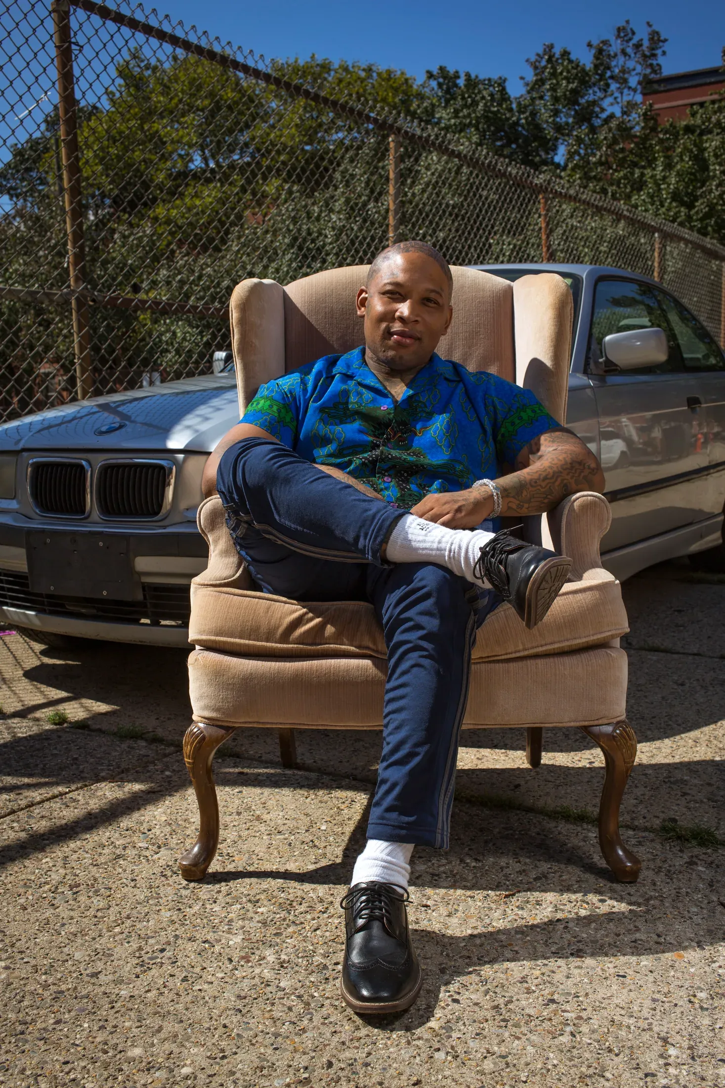 Environmental portrait of a man seated outdoors beside a blue vehicle.
