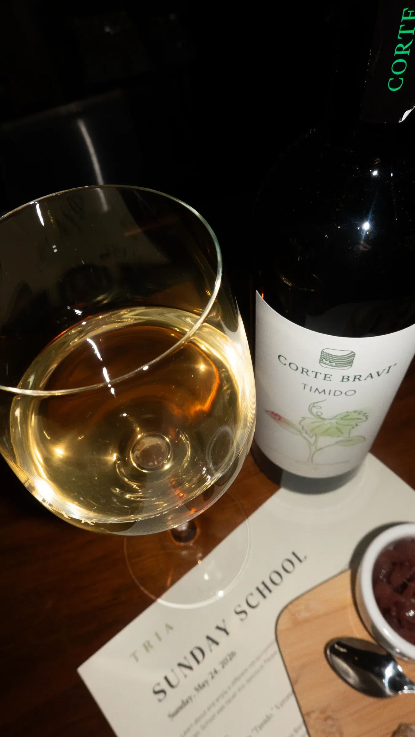 A glass and bottle of wine beside a Tria Sunday School menu.
