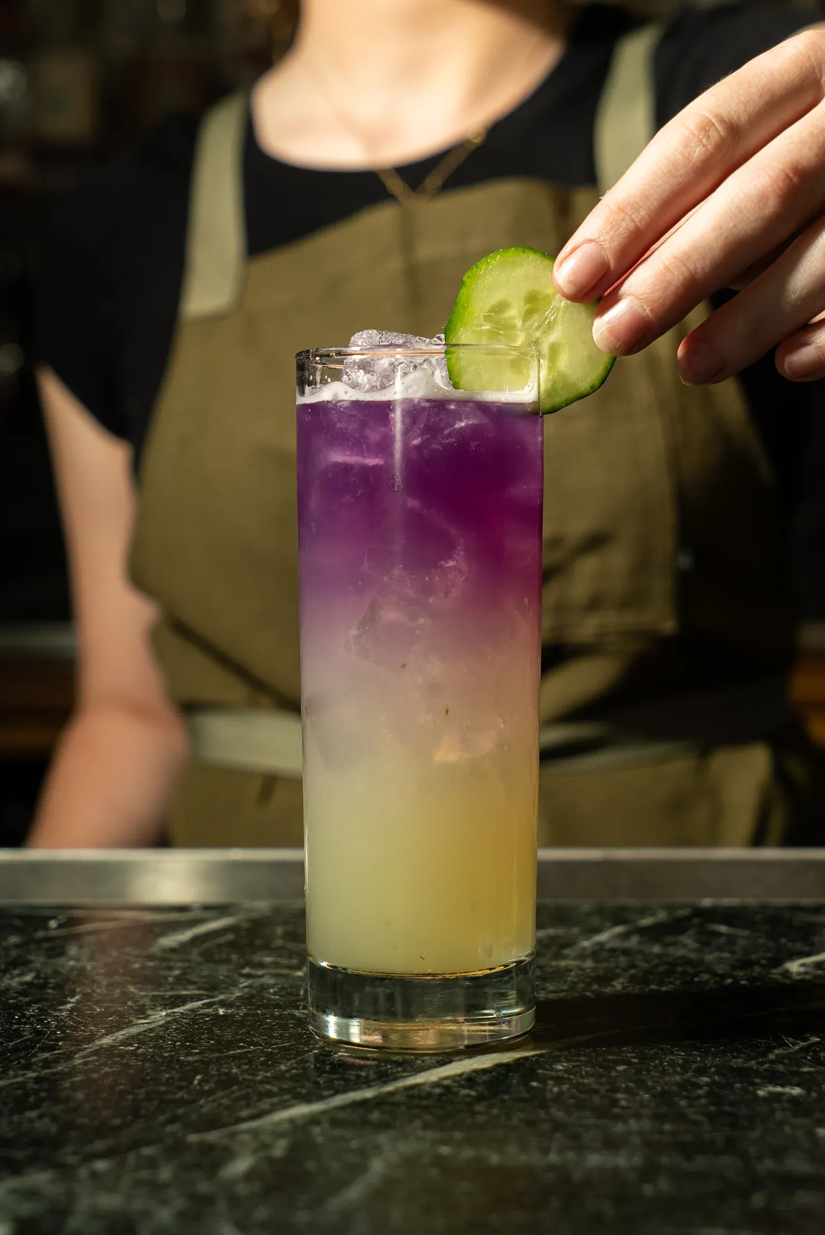 A bartender garnishing a purple and yellow layered cocktail.