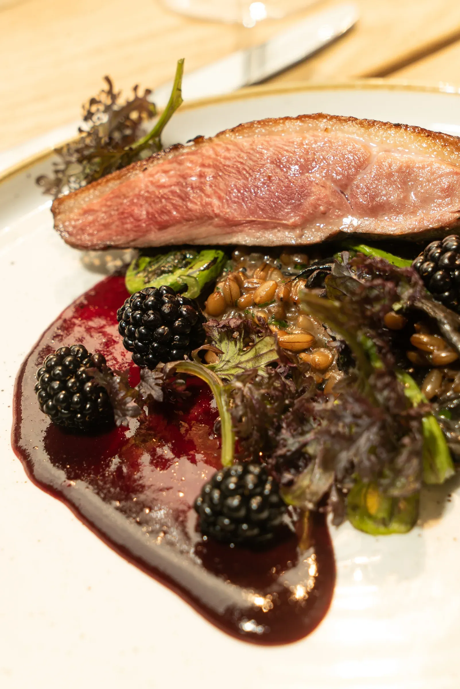 Sliced duck plated with blackberries and seasonal vegetables.