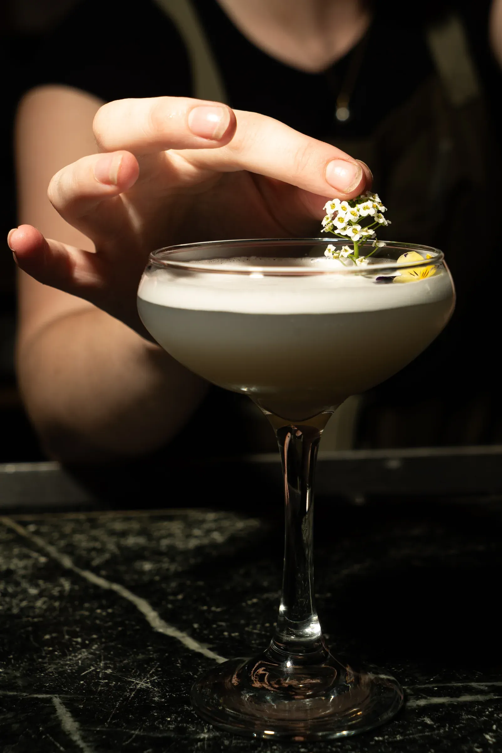 A bartender garnishing a pale cocktail served in a coupe glass.