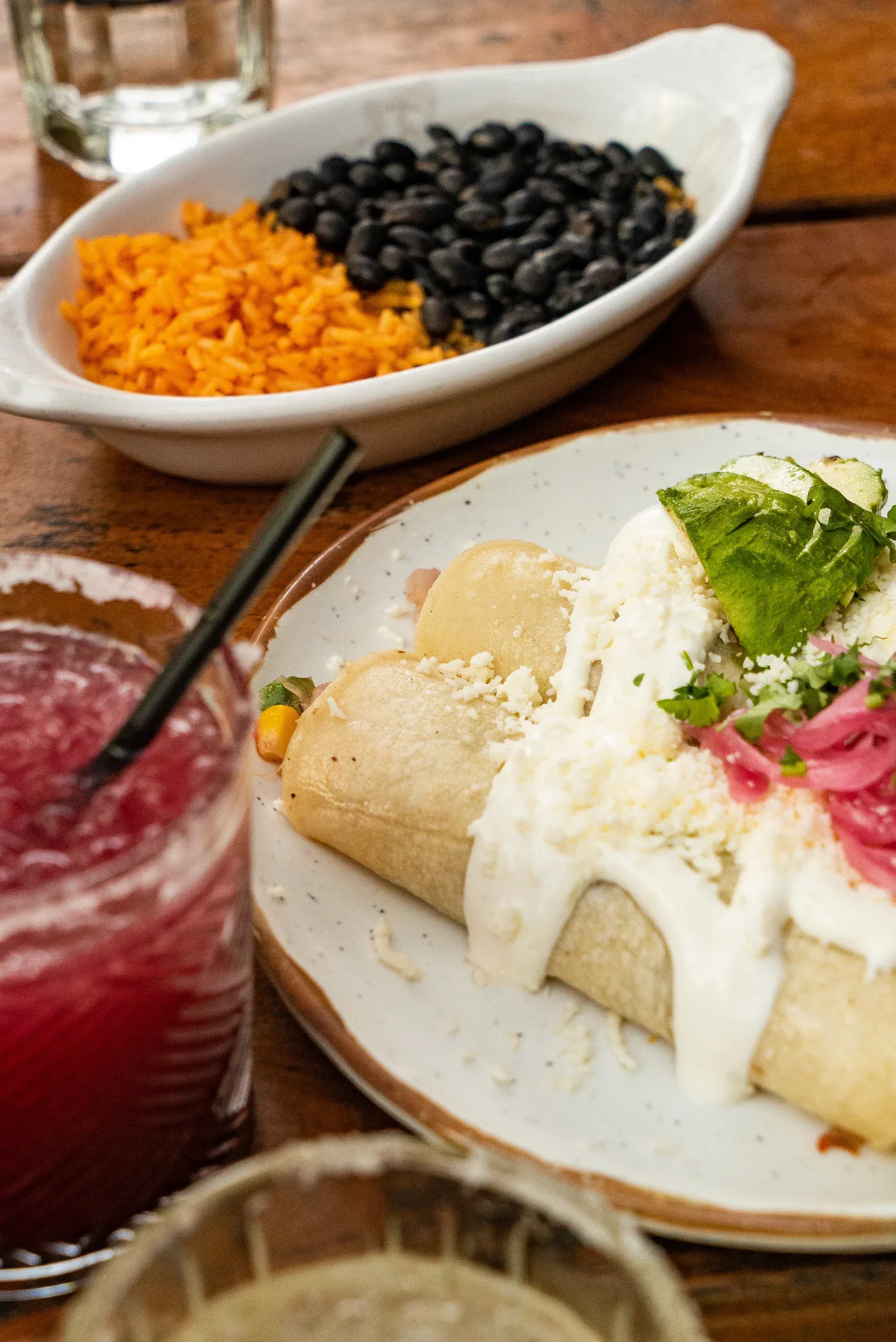 Enchiladas served with black beans, rice, and a red drink.