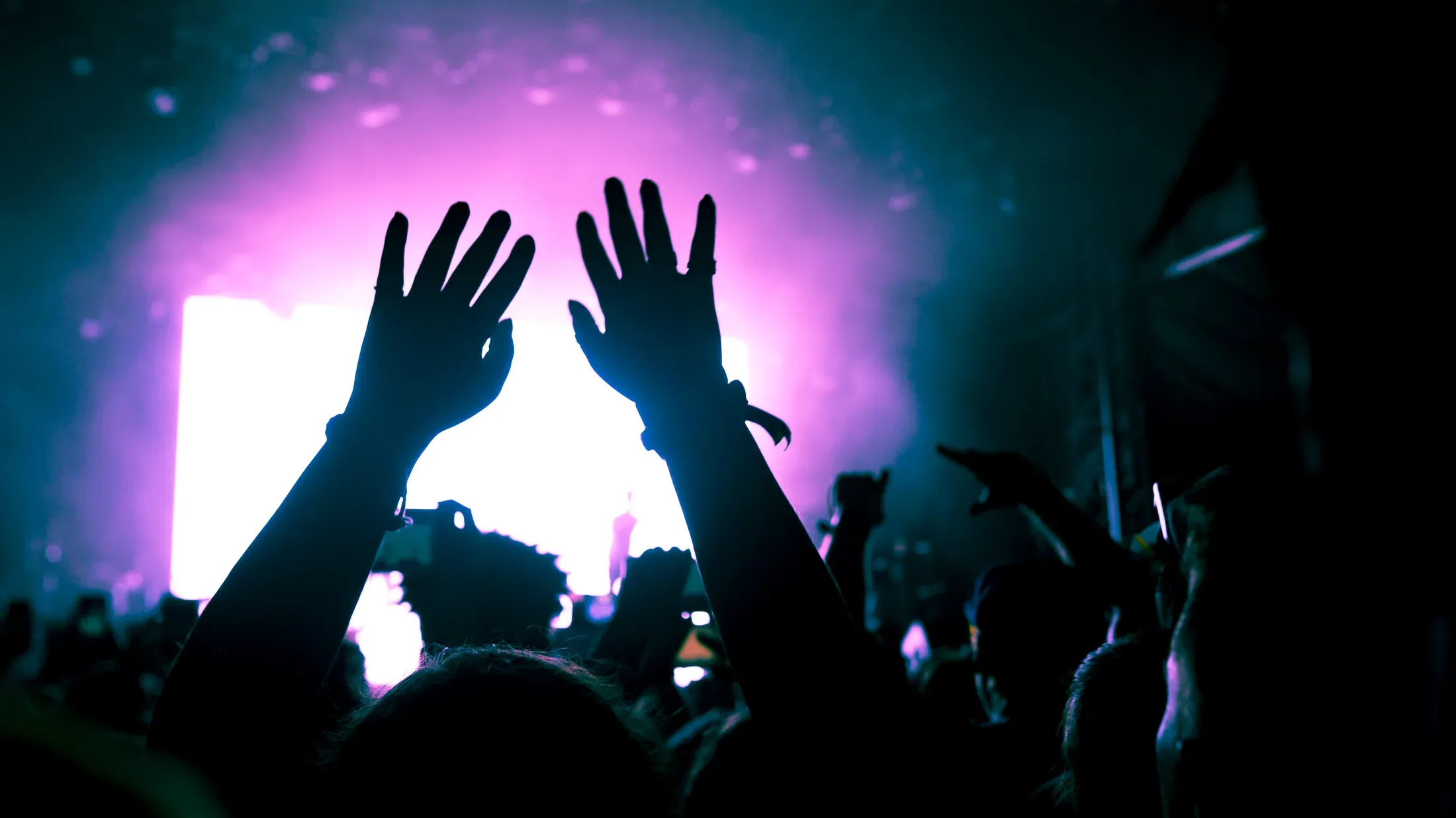 Raised hands silhouetted against a bright stage.
