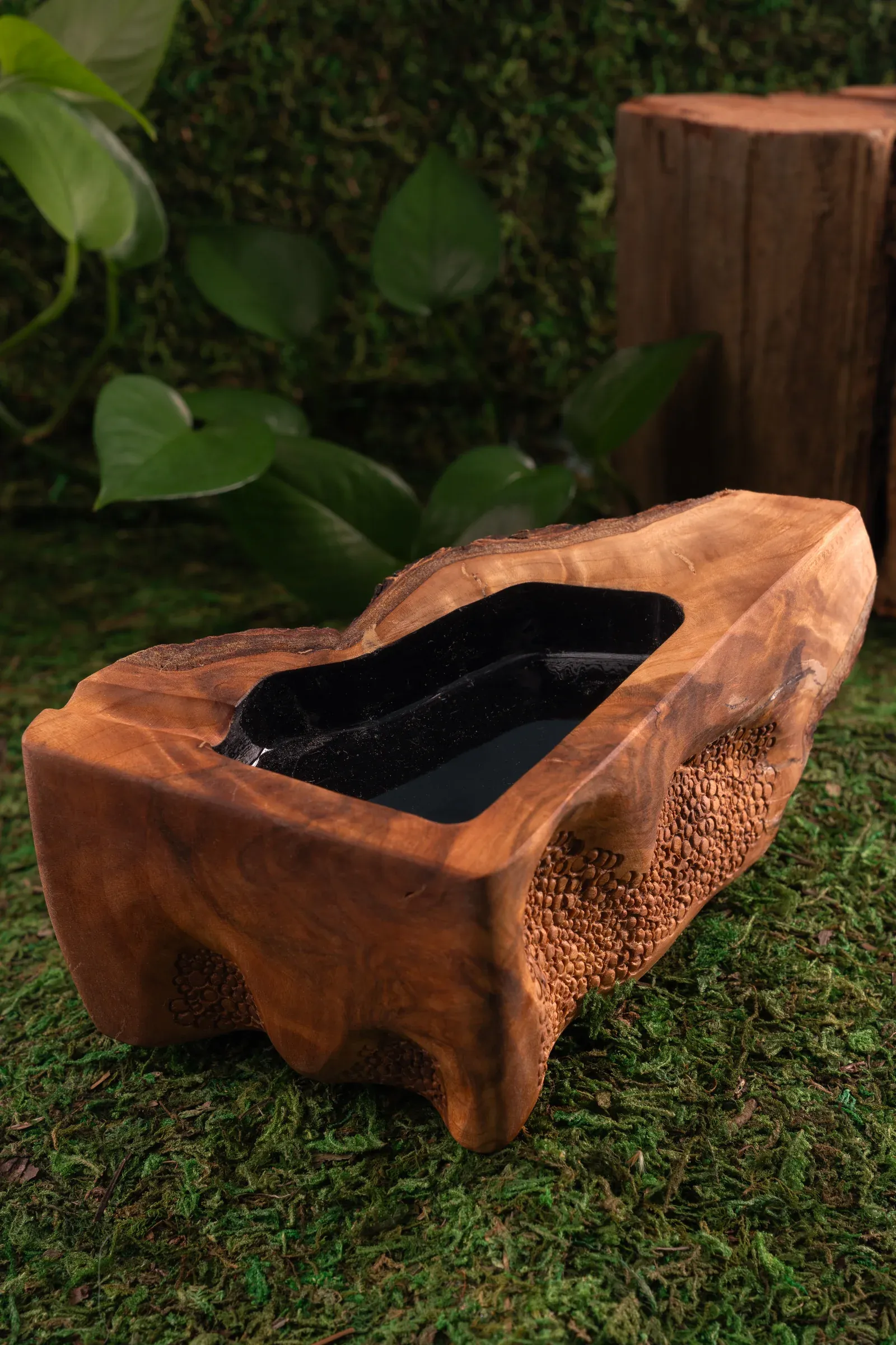 Sculpted wooden vessel photographed on a moss-covered set.