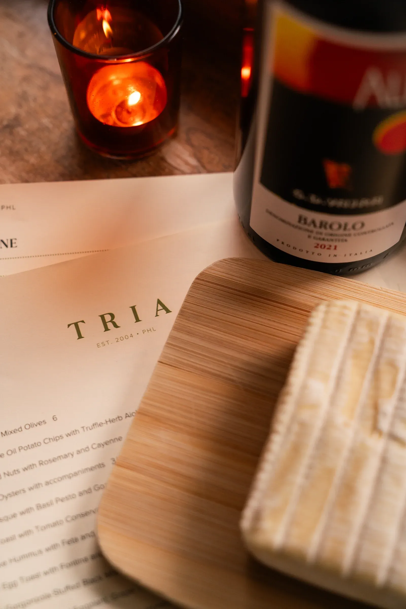 Barolo, cheese, candlelight, and a Tria menu arranged on a table.