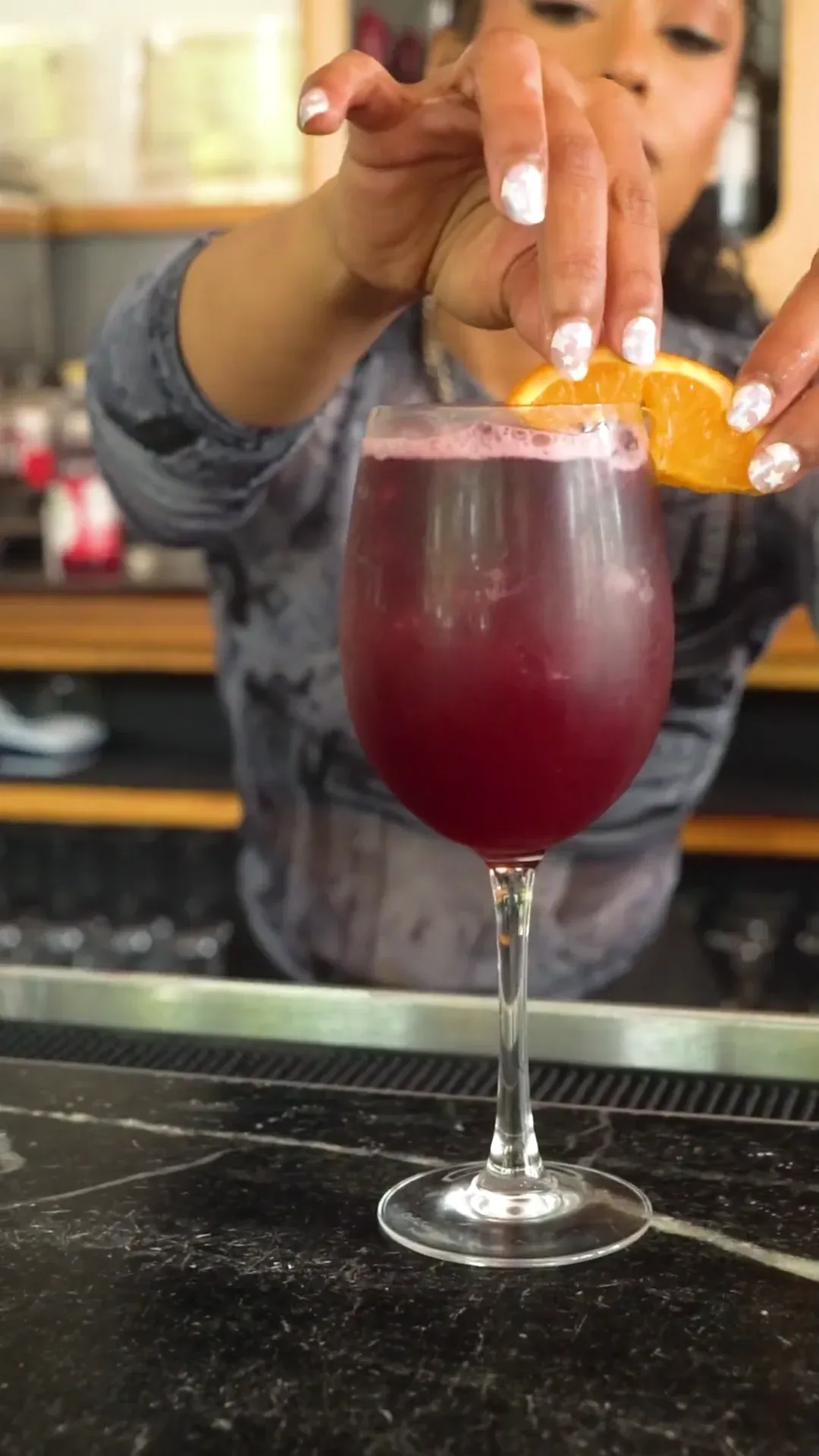 A bartender garnishing a deep red cocktail with citrus.