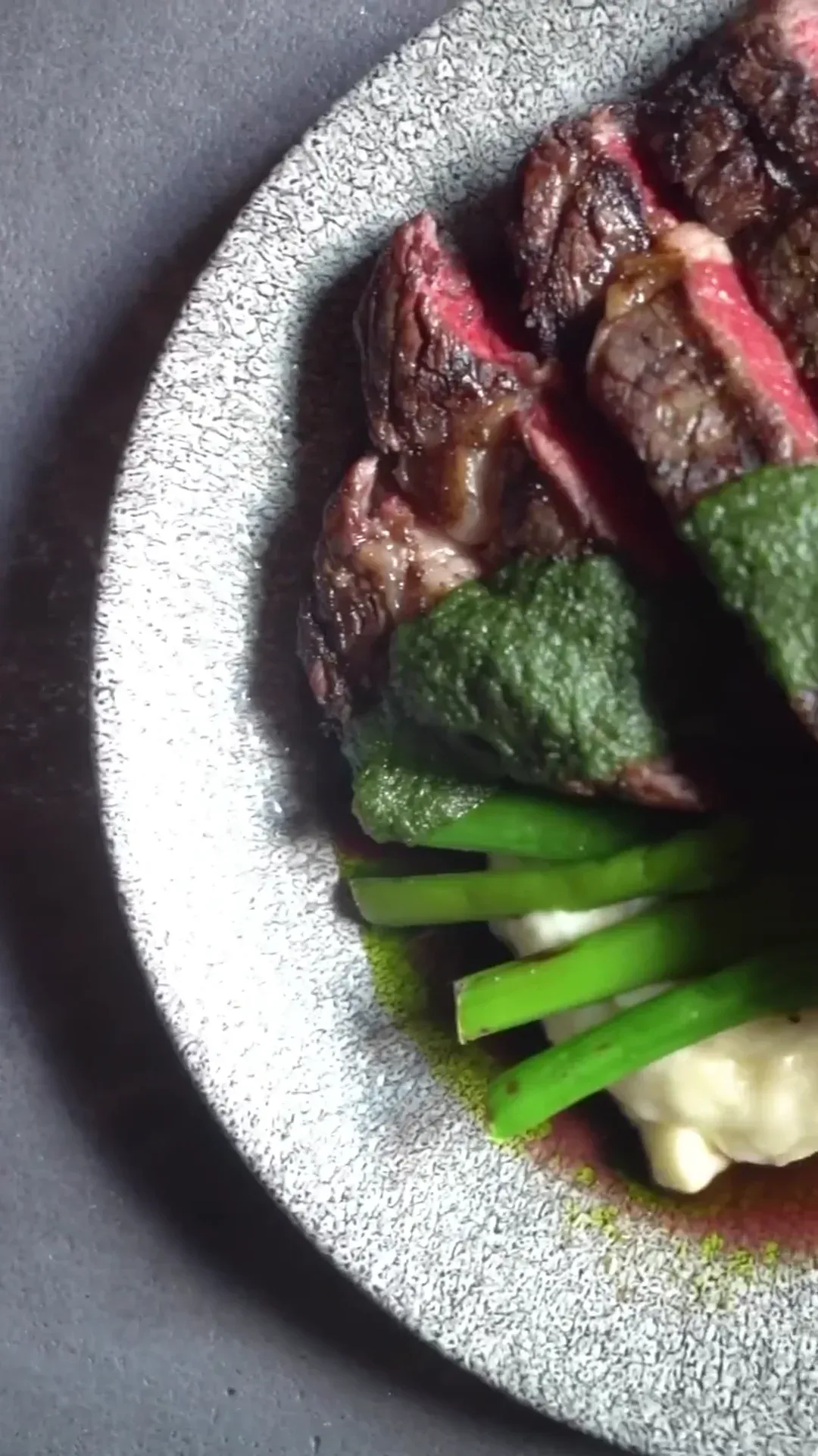 Sliced steak plated with greens and a vivid herb sauce.